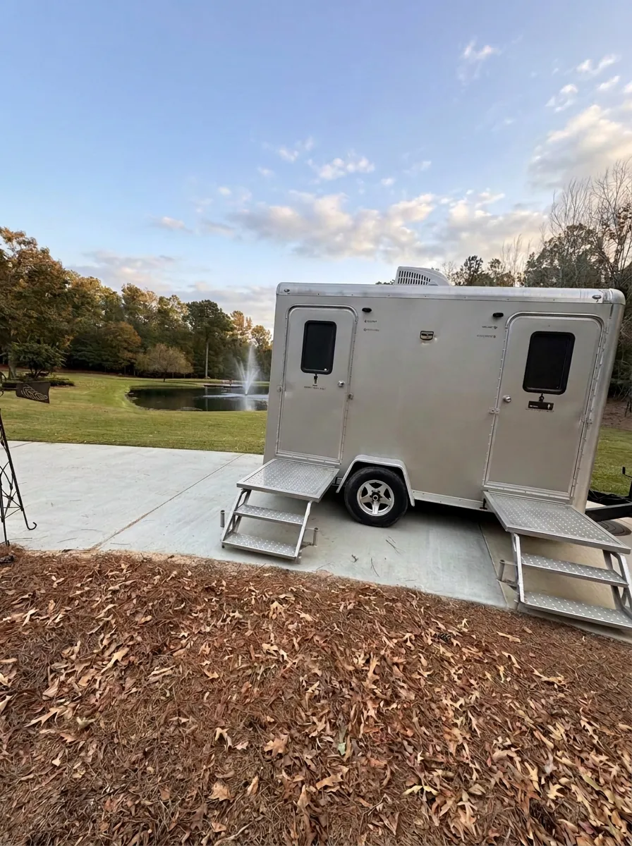 Augusta VIPee luxury restroom trailer with women's and men's doors, set up beside a pond with a fountain