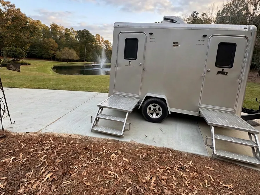 Augusta VIPee two-station luxury restroom trailer parked by a pond and fountain on a landscaped lawn