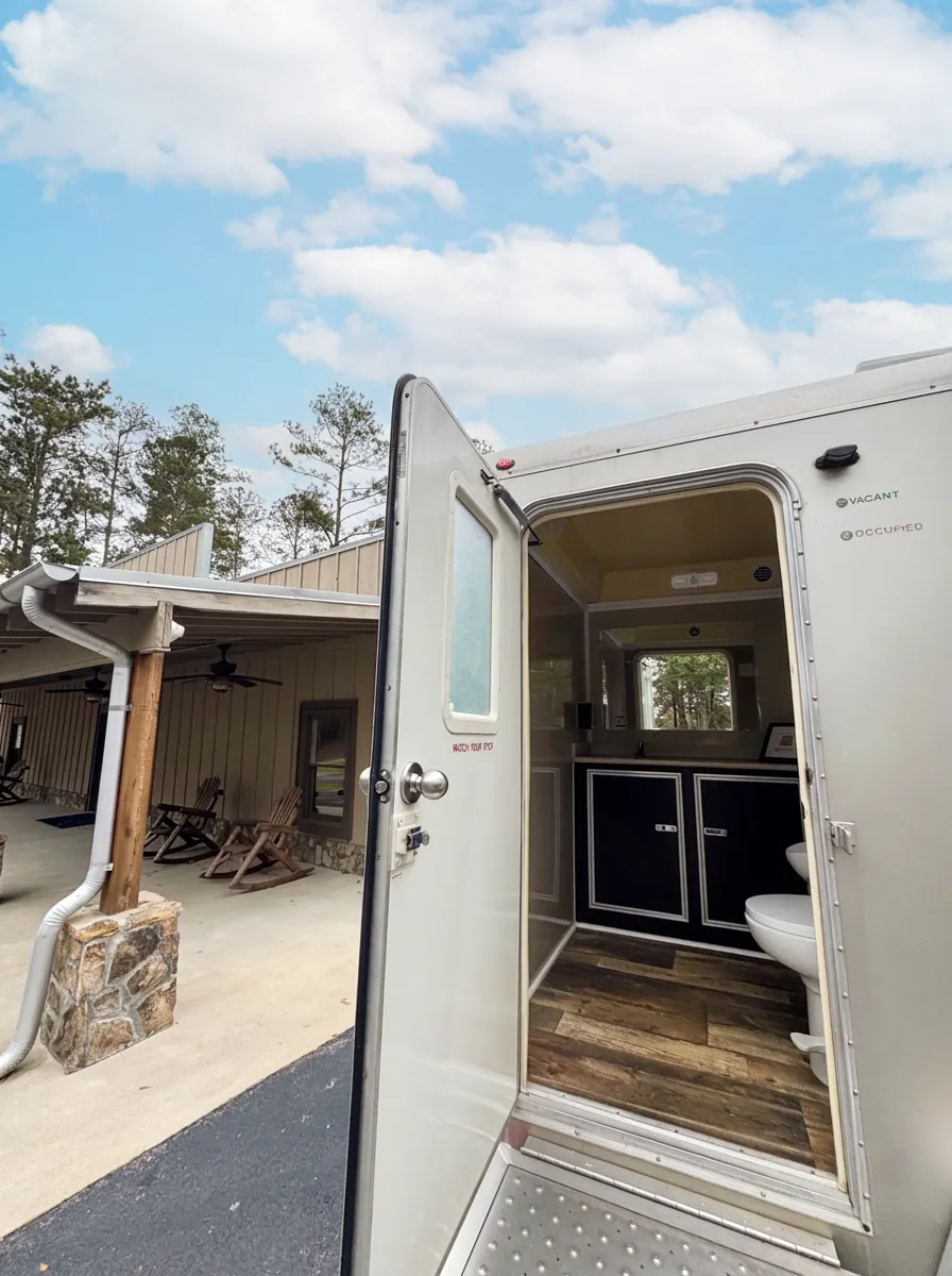 Inside an Augusta VIPee restroom trailer: wood-look floor, vanity cabinets with sink and mirror, flushing toilet